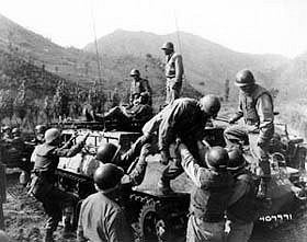 Photo:  Medical corpsmen of the 1st Battalion Aid Station, 31st Inf. Regt, 7th U.S. Inf. Div., assist in helping wounded infantrymen.