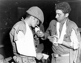 Photo:  Wounded infantrymen of Co L, 31st Inf. Regt., 7th U.S. Inf. Div., light up cigarettes after recieving first aid.