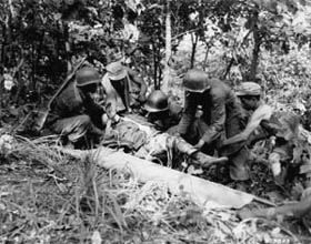 Photo:  Returning from an assault on Hill 717, men of Company "L", 7th RCT, 3rd Infantry Division, help a wounded buddy onto a strecher for evacuation to an aid station.