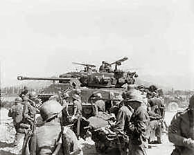 Wounded soldiers are evacuated (foreground) as M-4 tanks of the 5th RCT move to the front in the Kumchun area in Korea.